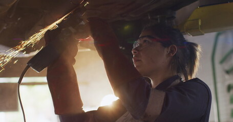 Young biracial individual wearing safety glasses working on car - Powered by Adobe