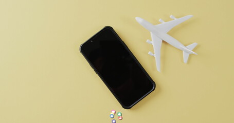 Smartphone near white plane model with colorful pills on yellow backdrop