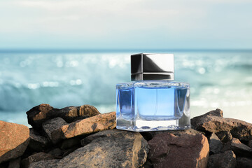 Bottle of aquatic perfume on stones near ocean. Fresh sea breeze scent