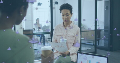 Image of connected icons over diverse female coworkers discussing reports while drinking coffee - Powered by Adobe