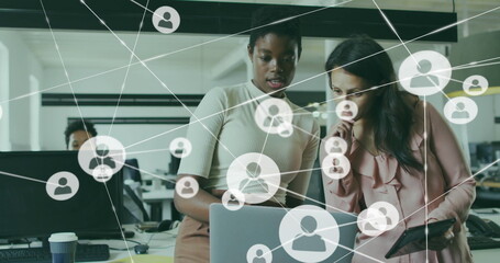 Image of connected icons over diverse female coworkers analyzing reports on laptop