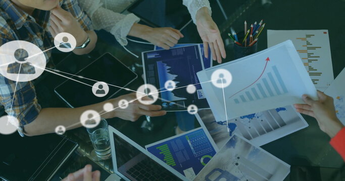 Image of connected icons over diverse coworkers discussing and analyzing reports in office