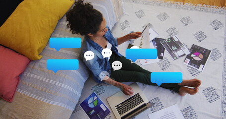 Image of social media bubbles over biracial woman working on laptop at home - Powered by Adobe