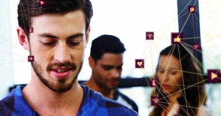 Image of two globes of digital icons over caucasian man smiling while using smartphone at office