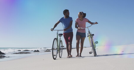 Image of light spots over african american couple with bicycles at beach