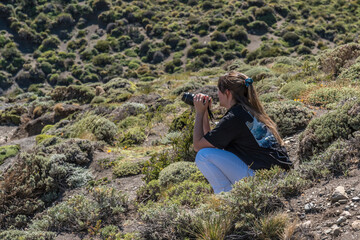 A woman is crouching down in a field, taking a picture with her camera
