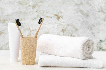 Holder with bamboo toothbrushes, clean towels and paste on light background