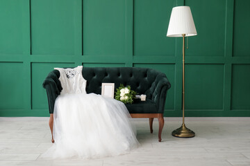 Wedding dress, bridal bouquet, ring box and photo frame on green velvet sofa in room