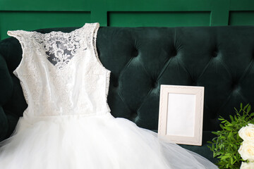 Wedding dress and photo frame on green velvet sofa near green wall