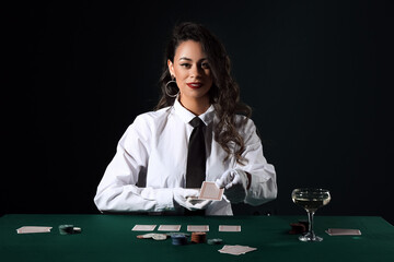 Beautiful African-American woman sitting at poker table with playing cards, chips and glass of...