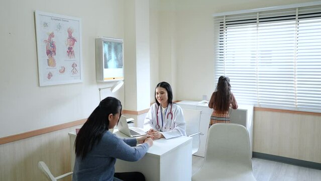 Asian medical pediatrician doctor female diagnosis hyperactive disorder in child symptoms and explain to mother in clinic, mom accepts treatment from physician while little girl running in room