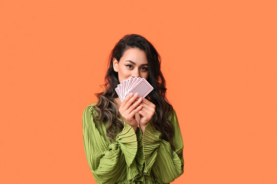 Beautiful young African-American woman with playing cards on orange background