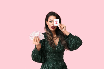 Surprised young African-American woman with playing cards and joker on pink background