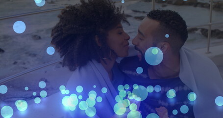 Fototapeta premium Image of glowing blue spots falling over african american couple embracing each other at beach