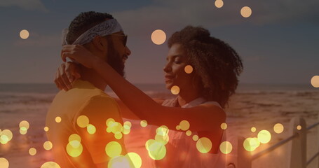 Fototapeta premium Image of glowing yellow spots over african american couple embracing each other at the beach