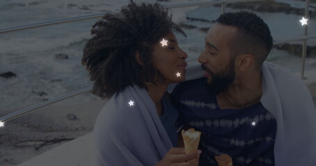 Fototapeta premium Image of glowing star icons over african american couple embracing each other at the beach