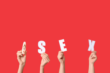 Female hands with word SEX and vibrator on red background