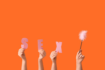Female hands with word SEX and feather stick on orange background