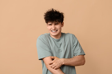 Young man with allergy scratching himself on beige background