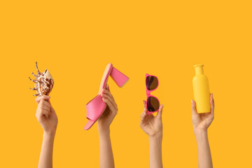 Female hands with seashell, sunscreen, sunglasses and heeled sandal on yellow background. Travel...