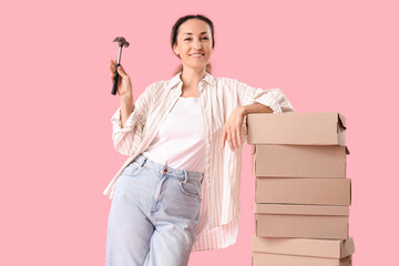 Happy female shoemaker with hammer and boxes on pink background