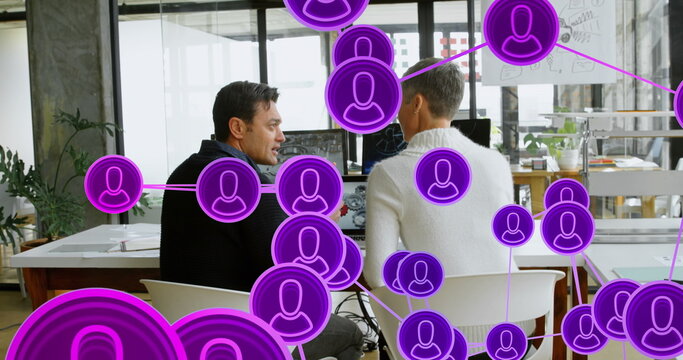 Image of connected icons with lines over diverse coworkers discussing reports in office