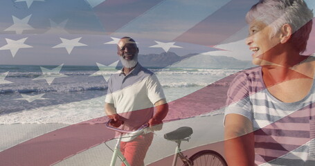 Image of flag of usa over happy senior biracial couple with bikes on beach