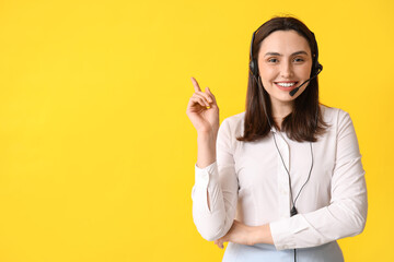 Female technical support agent in headset pointing at something on yellow background