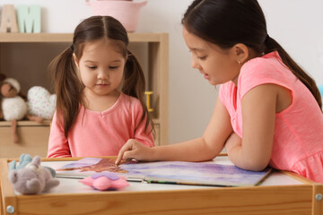 Cute little Asian happy sisters with toys reading book at table in child room