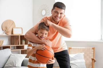 Young man and his little son playing with basketball ball at home
