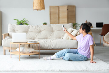 Young African-American woman turning on air conditioner at home