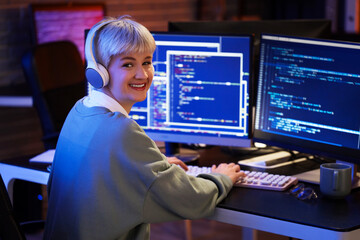 Female programmer with headphones working in office at night