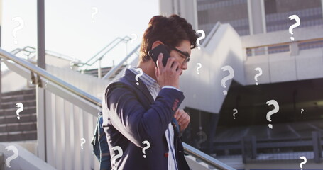 Image of question marks over asian businessman talking on cellphone while moving down steps