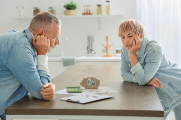 Sad mature couple counting money at table in kitchen