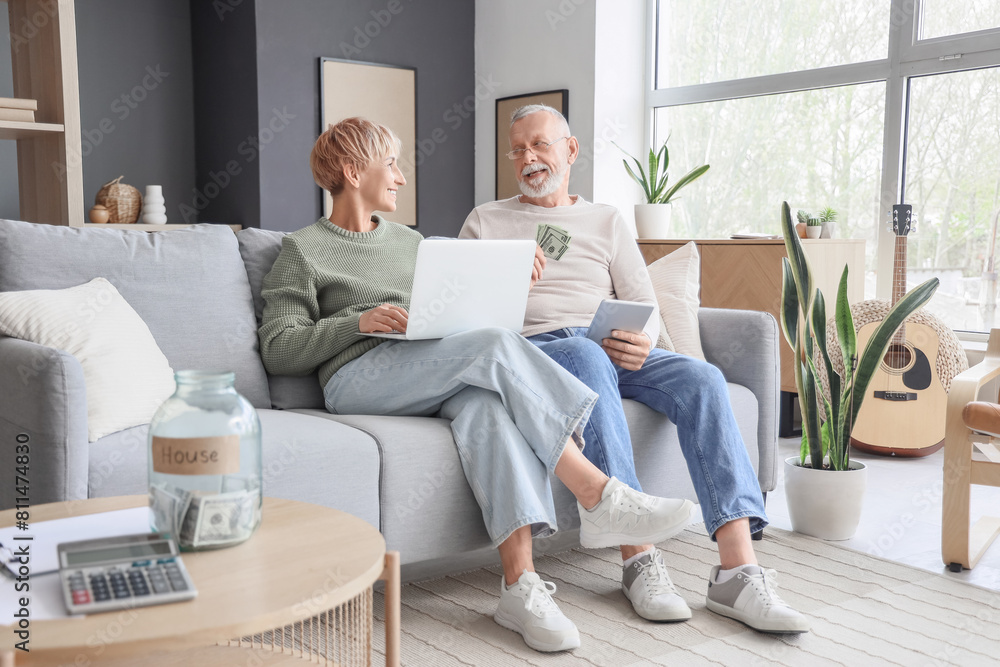 Wall mural Mature couple with money and modern gadgets sitting on sofa at home