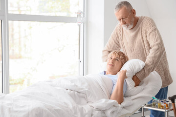Mature man adjusting his sick wife's pillow in clinic