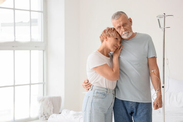 Mature man with infusion drip hugging his wife in bedroom
