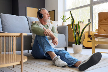 Mature man in headphones listening to music on floor at home