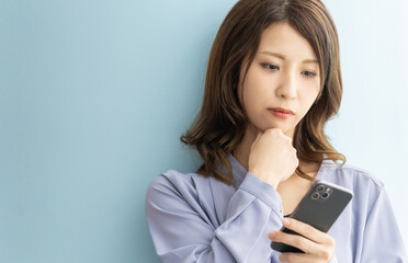 Naklejka premium スマートフォンを見て真剣な表情で考える日本人女性