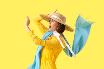 Young woman in hat with strong wind on yellow background