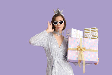 Beautiful woman in crown with party blower and Birthday gifts on lilac background
