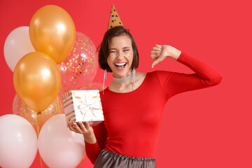 Beautiful woman in party hat with Birthday gift and balloons on red background