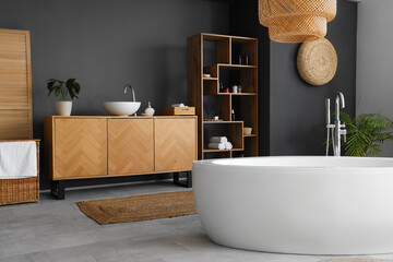 Interior of modern bathroom with bathtub, wooden furniture and houseplants