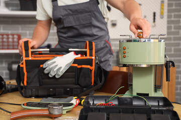 Male worker with bag of tools repairing coffee machine in workshop, closeup