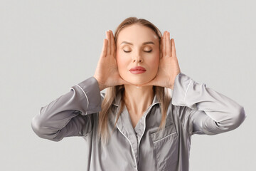 Beautiful woman in pajamas doing face building exercise on light background