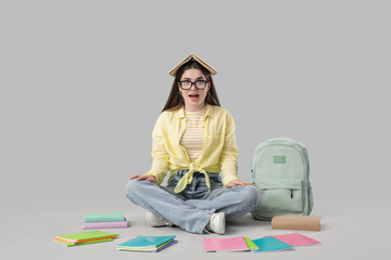 Female student with books sitting on light background