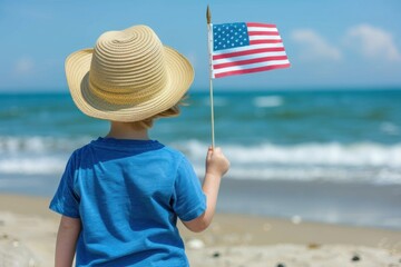 A young Caucasian boy, viewed from behind, holds an American flag on a sunny beach day, wearing a blue shirt and straw hat. 4th of July, american independence day, , memorial day concept