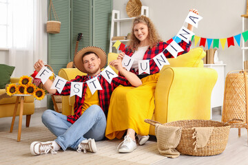 Happy young couple holding bunting with text FESTA JUNINA at home