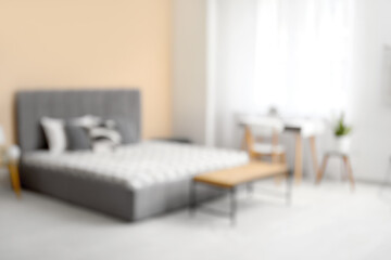 Stylish bedroom with bed, bedside table and workplace, blurred view