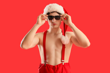 Young man in Santa hat with sunglasses on red background. Christmas in July